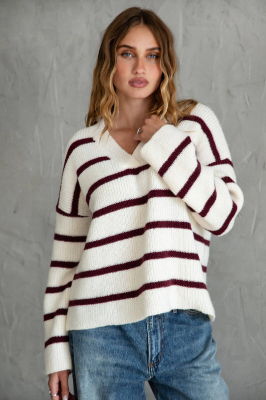 Woman wearing a white and red striped sweater with blue jeans against a gray background